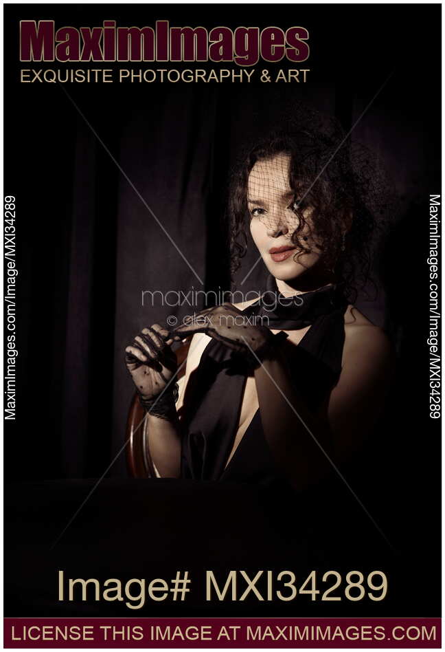 Portrait of beautiful mysterious femme fatale lady dressed in black wearing veiled hat taking off her gloves