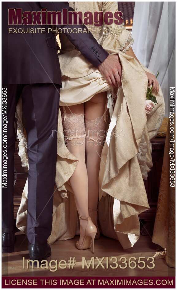 Rear view of a man raising up woman's dress skirt revealing her sexy legs in stockings on high-heel shoes