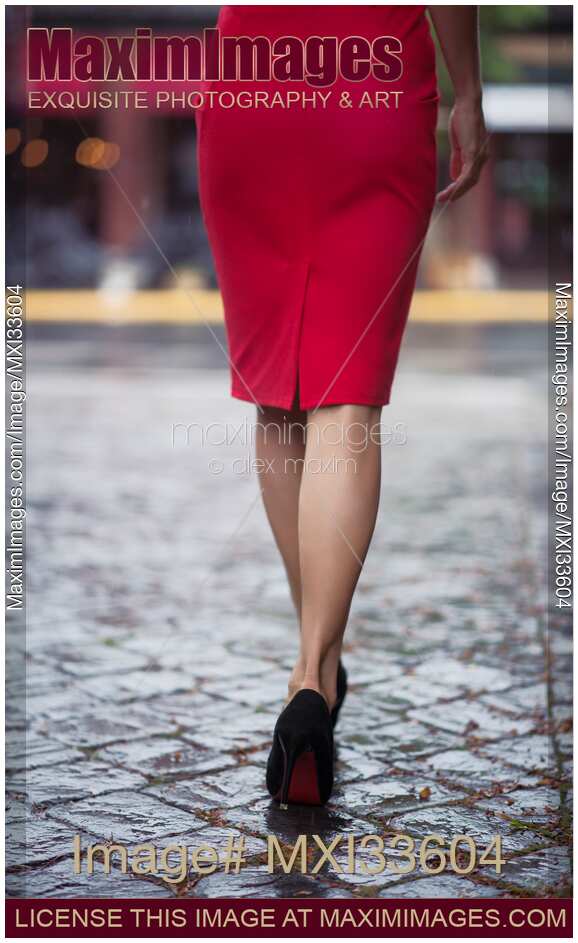 Rear view of a sexy woman in red dress and high heel shoes walking on a wet cobbled city street in the rain