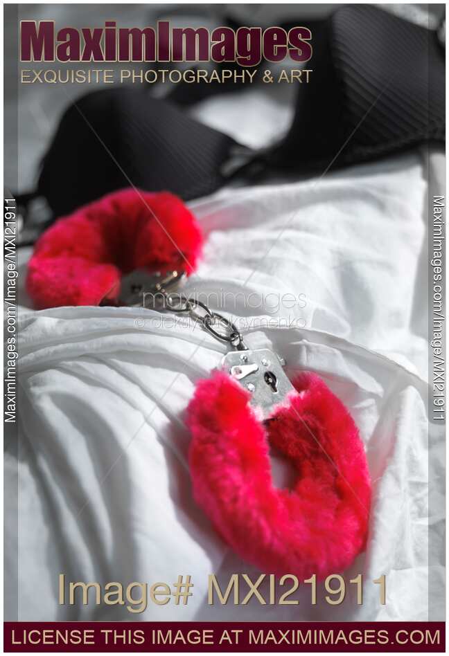 Red Handcuffs and a bra on white bed sheets