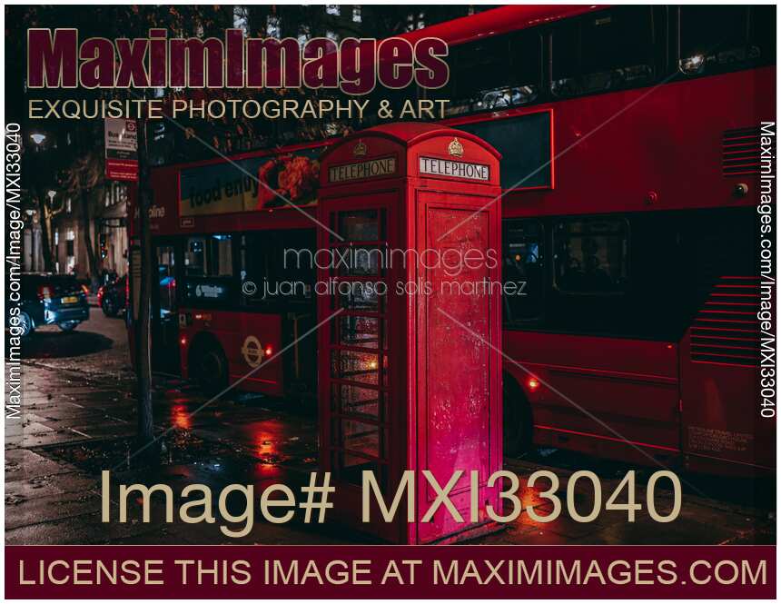 Red telephone booth and city bus on night street after rain in London England