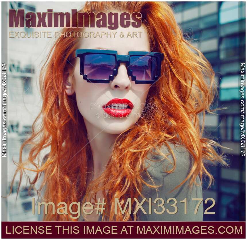 Retro fashion portrait of a young red-haired lady in funky avant-garde sunglasses on a city rooftop
