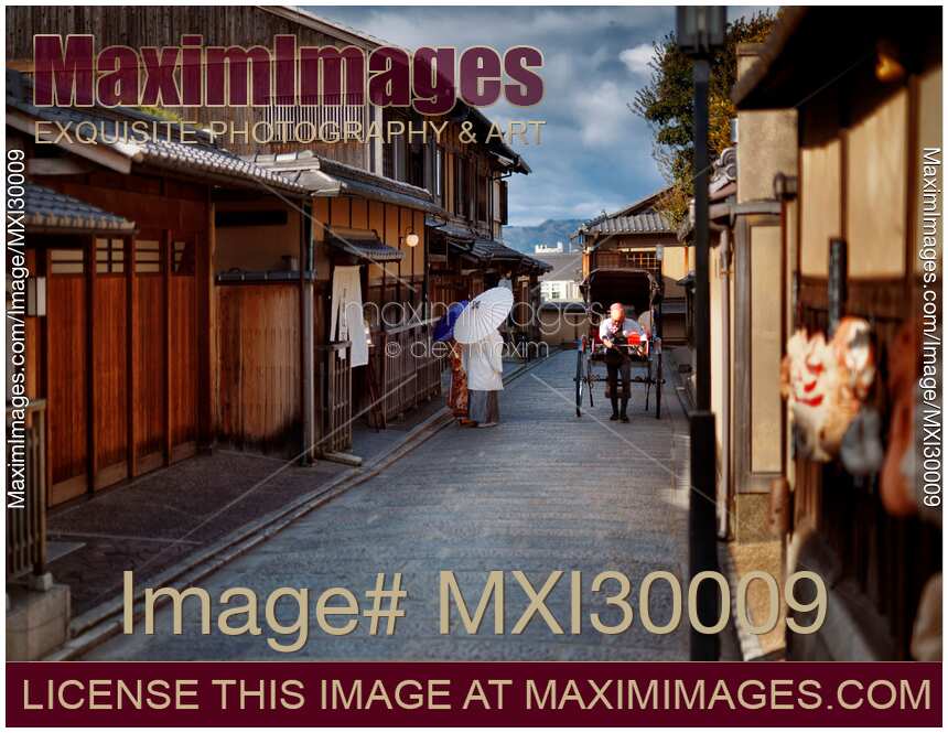 Rickshaw passing a Japanese couple wearing traditional kimono walking down an old street in Kyoto