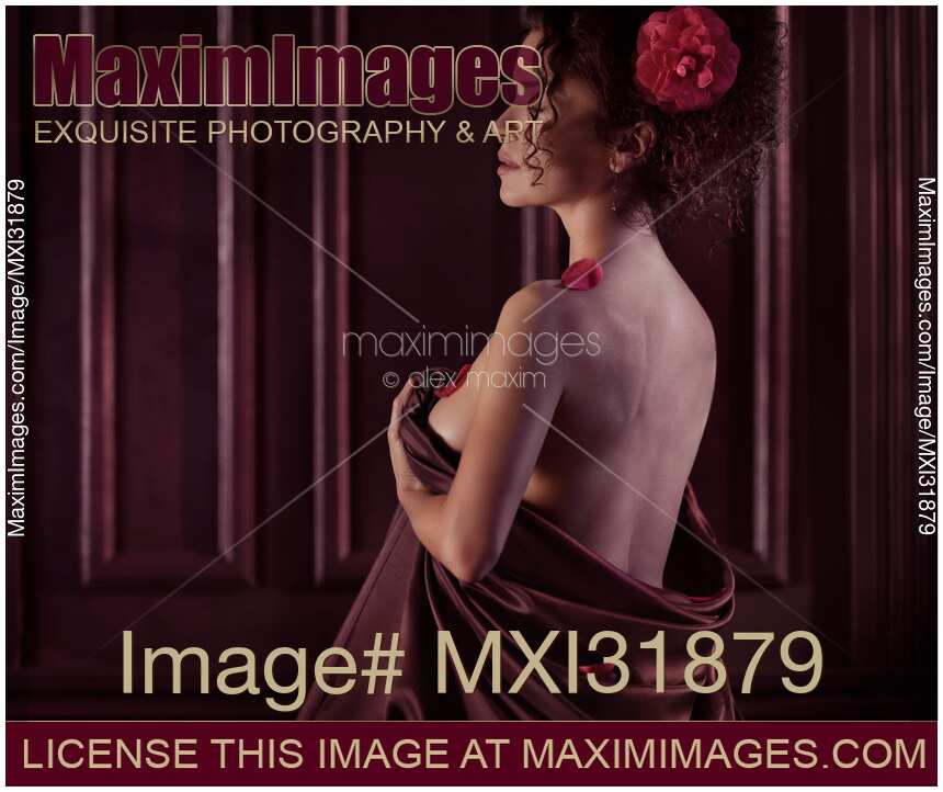 Romantic boudoir portrait of woman with flower in hair wrapping in bed sheets