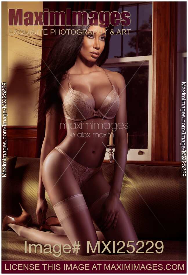 Romantic glamour portrait of a beautiful black woman in beige lingerie and stockings posing on a bed
