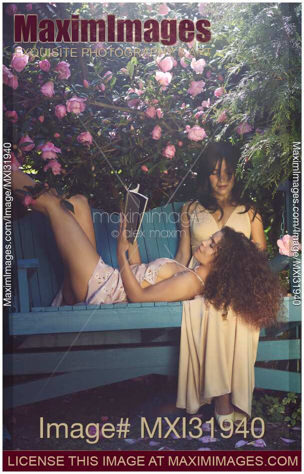 Romantic lesbian couple resting on a bench in a garden woman reading a book lying on lap of another