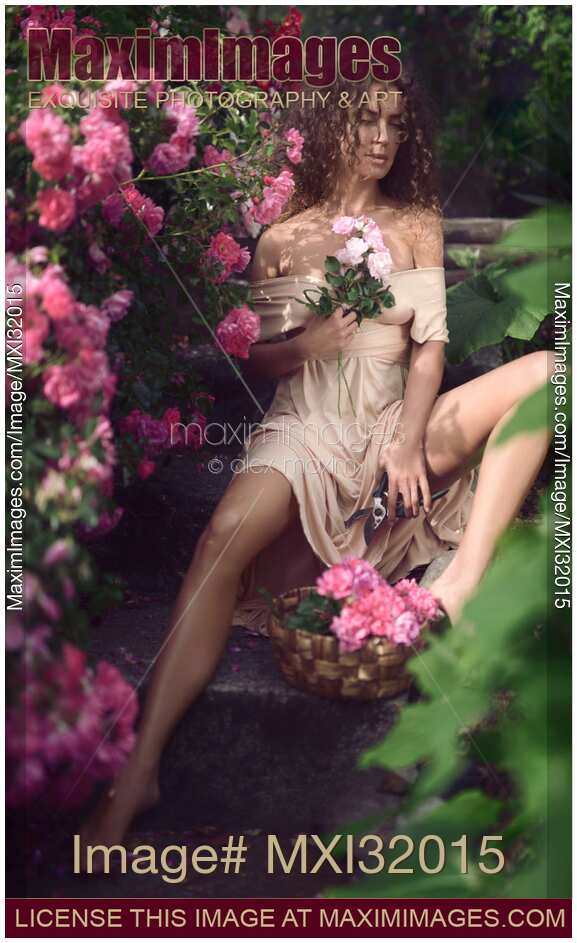 Romantic portrait of a woman in a garden sitting in a sensual relaxed pose with freshly cut pink roses in her hand