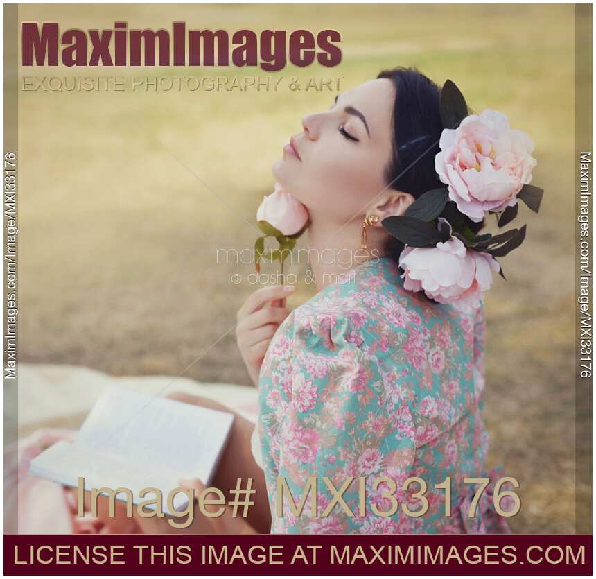 Romantic sensual portrait of a beautiful woman with pink flowers in her hair reading a book outdoors in a park