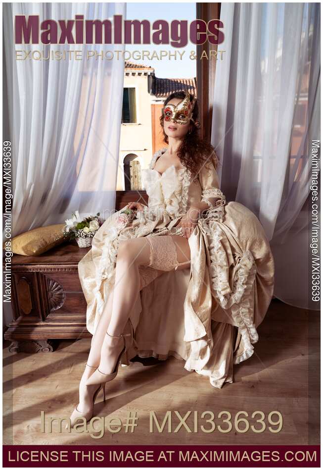 Seductive Venetian lady in carnival mask and beautiful vintage dress revealing her sexy legs in stockings at masquerade ball