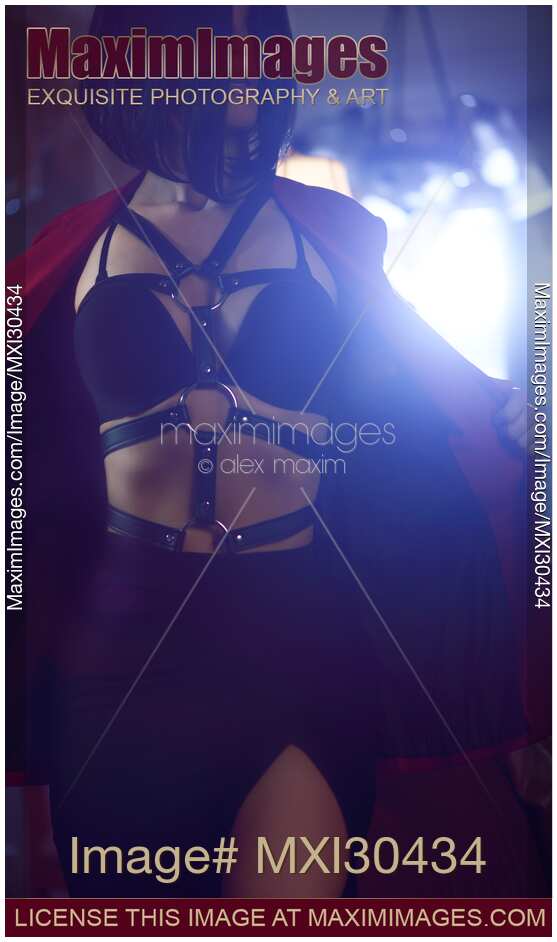 Seductive woman with undressing revealing sexy bondage leather harness and underwear in dim light