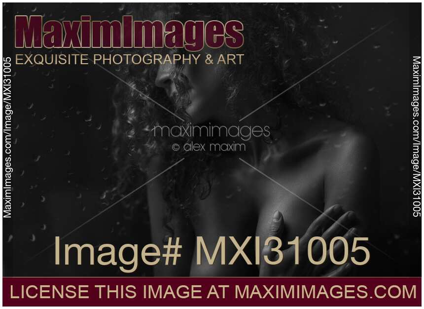 Sensual art nude black and white portrait of a woman covering her breasts behind wet window in night light