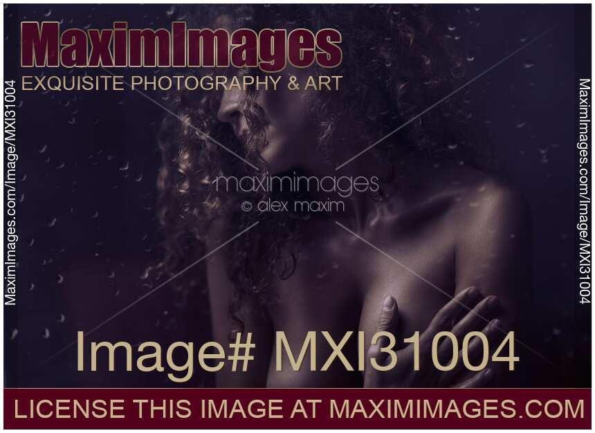 Sensual art nude portrait of a woman covering her breasts behind wet window in dim night light