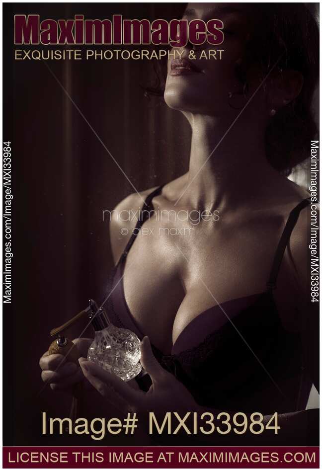 Sensual beauty portrait of a woman in lingerie spraying perfume on her chest from a bottle