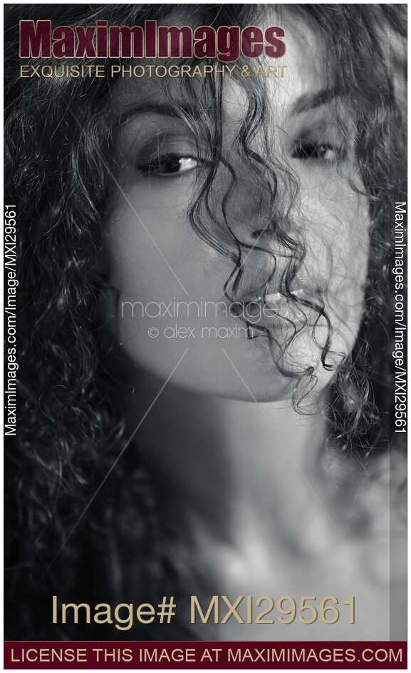 Sensual black and white beauty face portrait of a young woman looking through her curly hair