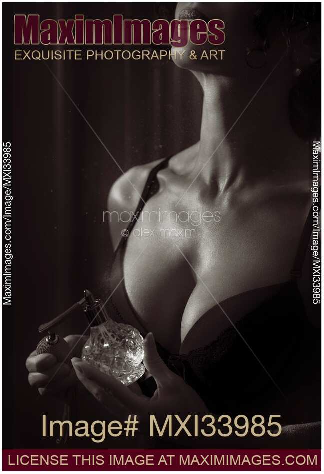 Sensual black and white beauty portrait of a woman in lingerie spraying perfume on her chest from a bottle