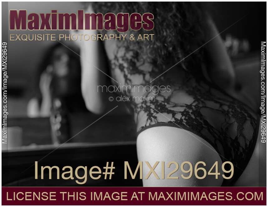 Sensual black and white boudoir closeup of woman in sexy underwear leaning towards the mirror applying lipstick
