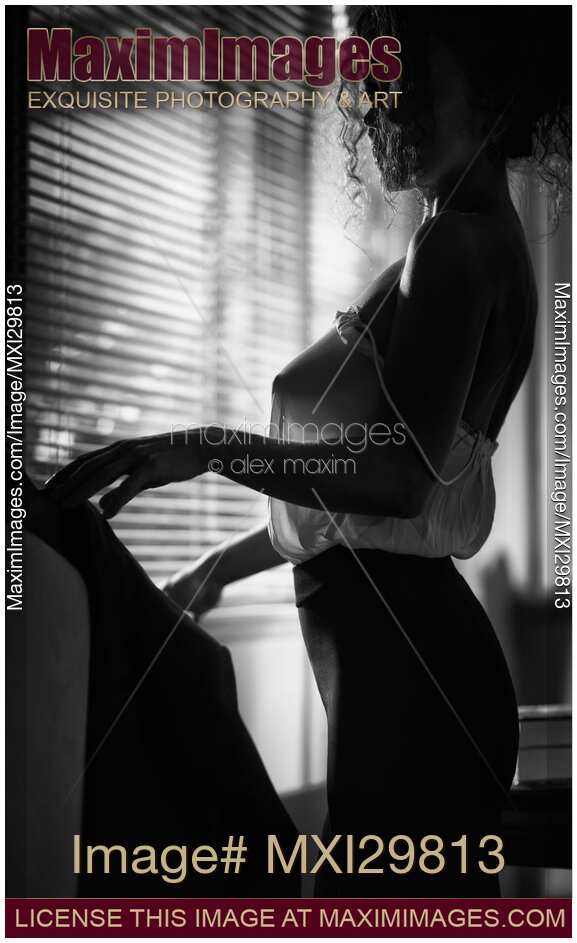 Sensual black and white boudoir portrait of woman in sexy sheer blouse standing by the window
