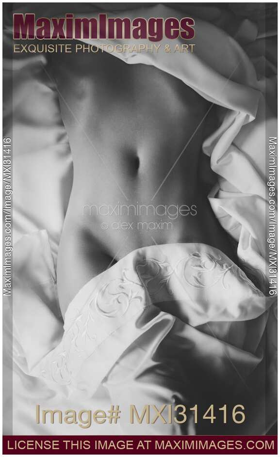 Sensual black and white of a nude woman body partially uncovered in bed revealing her naked stomach