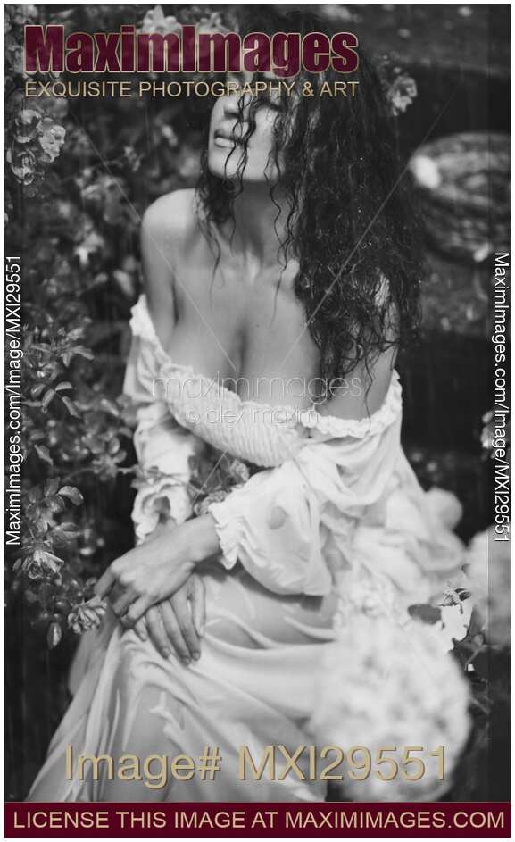 Sensual black and white portrait of a beautiful woman in wet clothes sitting in rose garden in the rain