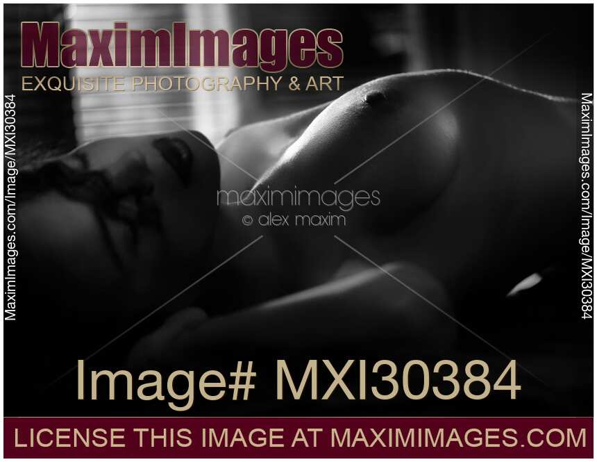 Sensual black and white portrait of a nude woman lying down closeup of her cheast in dim light implying making love