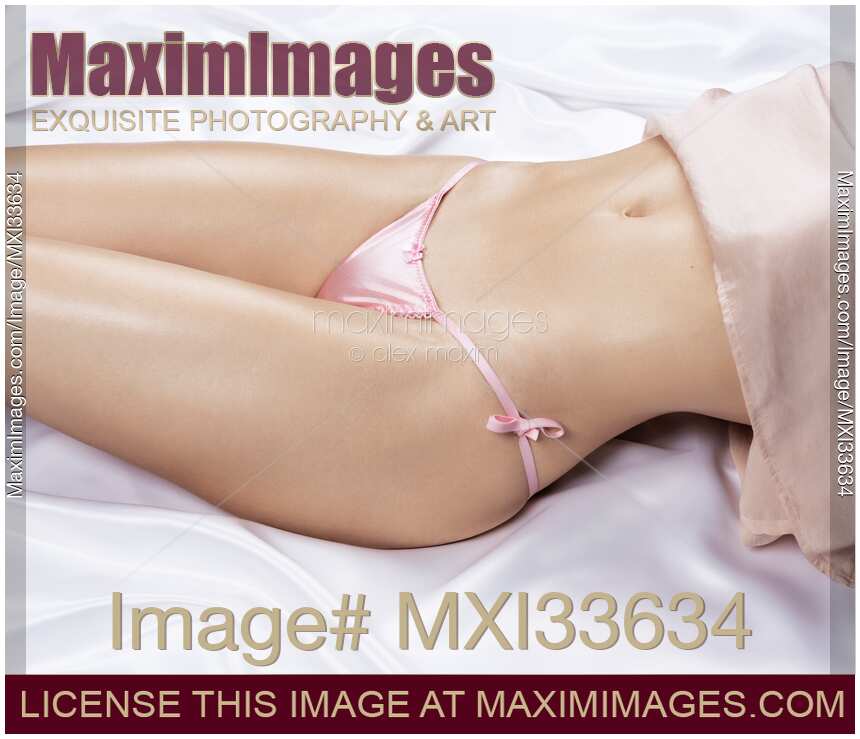 Sensual boudoir closeup of a woman with sexy curves and glowing skin in pink underwear lying on white satin bed