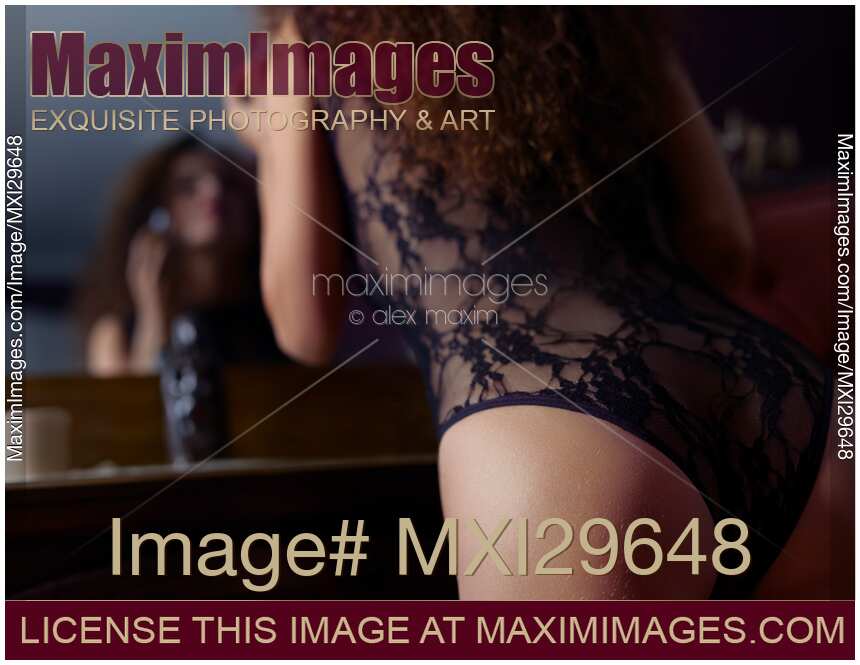 Sensual boudoir closeup of woman in sexy underwear leaning towards the mirror applying lipstick