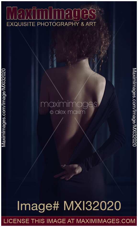Sensual boudoir portrait a woman in black dress with low cut pulling it down revealing her back in dim mysterious light