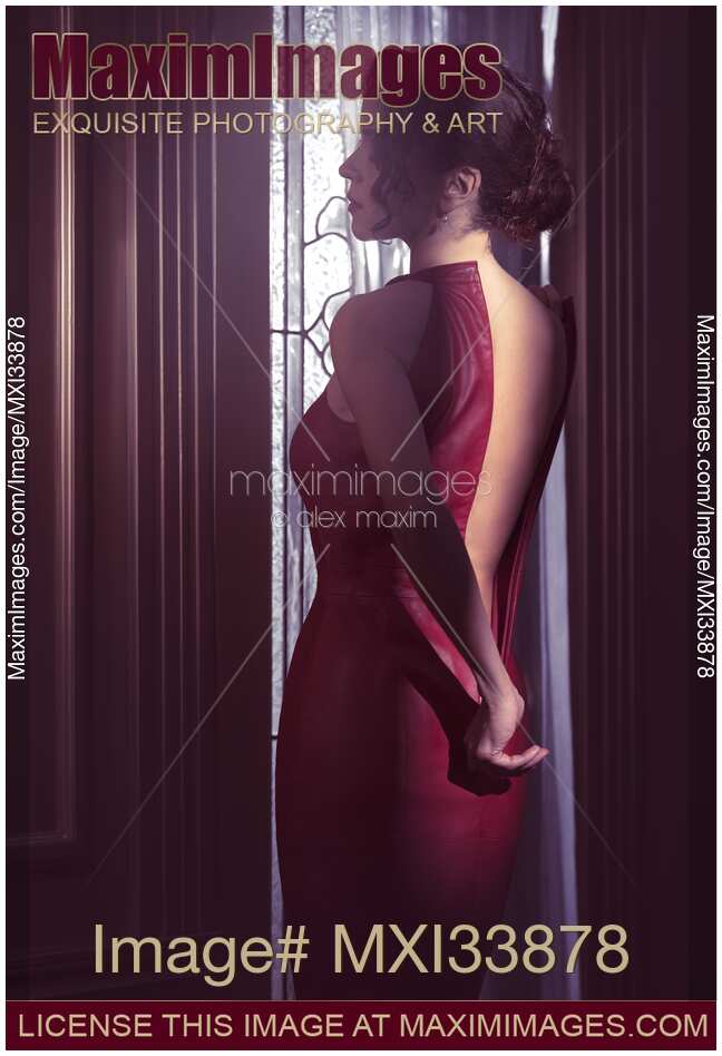 Sensual boudoir portrait a woman in red leather dress pulling down zipper closure revealing her bare back in dim indoor night light