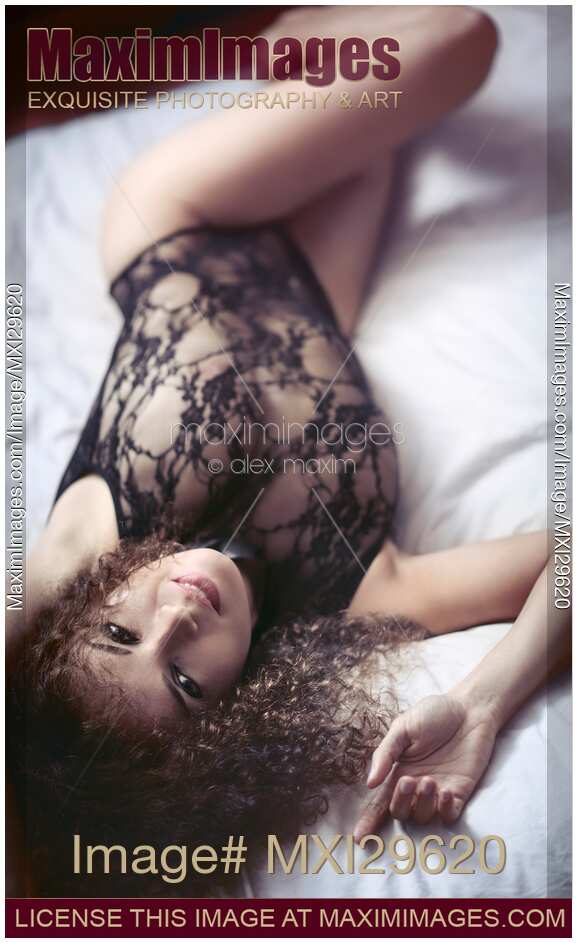 Sensual boudoir portrait of a smiling young woman lying on bed in lacy underwear