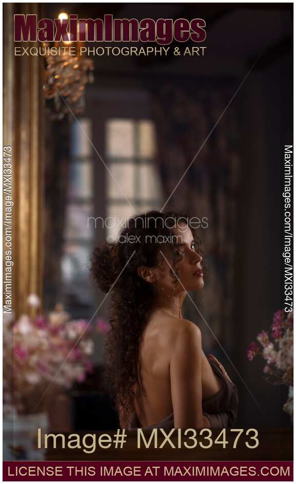 Sensual boudoir portrait of a woman taking her dress off looking at a mirror of a dark vintage house