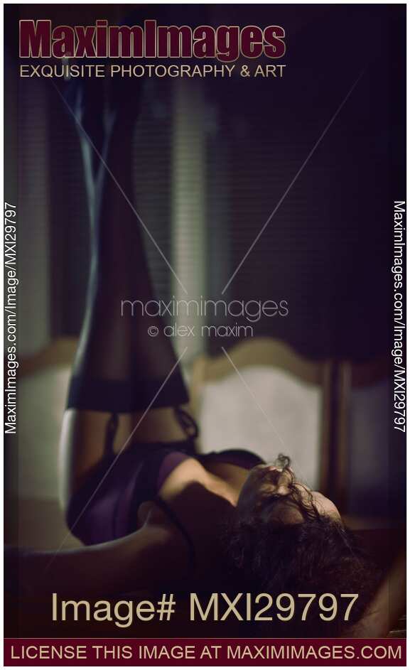 Sensual boudoir portrait of sexy woman lying on table in corset and stockings with her legs raised up