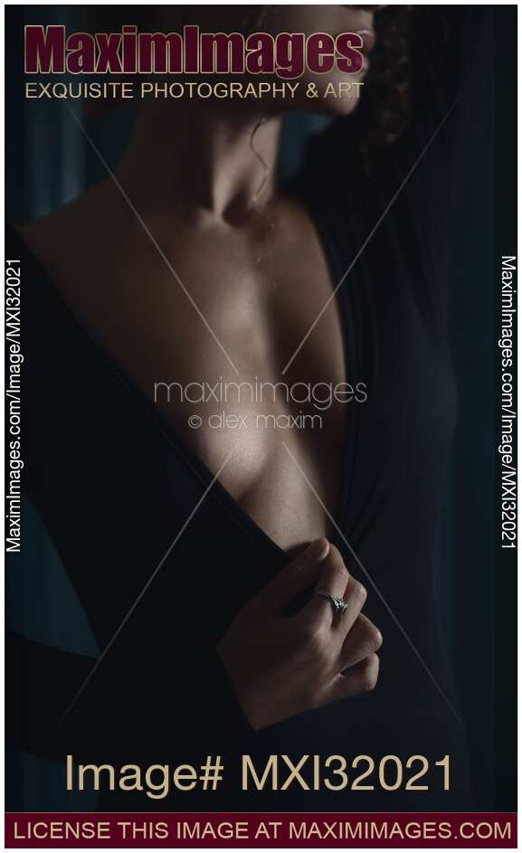 Sensual closeup of a woman in a black dress with a low-cut cleavage revealing her chest in dim dramatic light