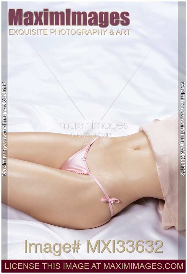 Sensual closeup of a woman sexy body with delicate curves and shiny skin in pink underwear lying on white satin bed