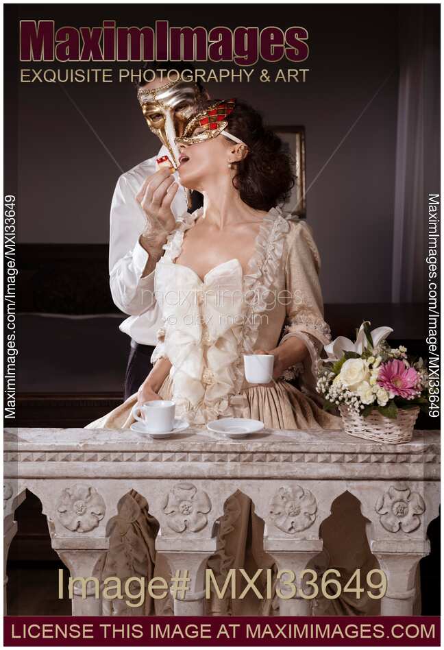 Sensual couple portrait of masked man tempting beautiful lady in vintage Venetian carnival dress and mask with pastry. Casanova.