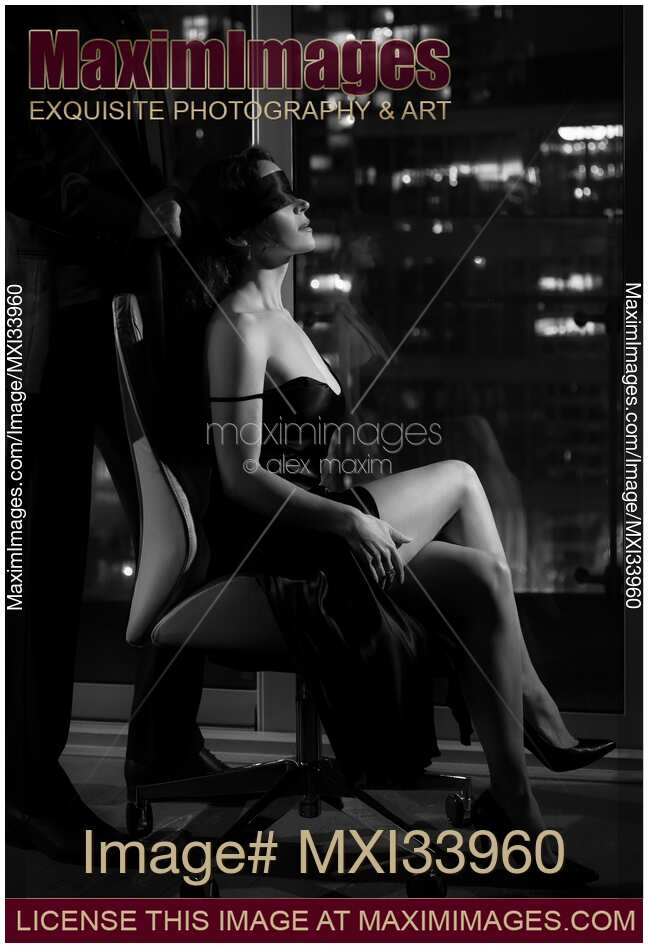 Sensual elegant couple black and white. Man tying blindfold on beautiful sexy woman sitting in a chair by a window with night city view.