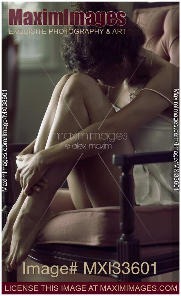 Sensual emotional portrait of young woman in night shirt sitting in armchair with her head on her knees