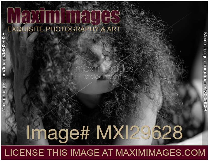Sensual expressive black and white portrait of a woman lying on a bed her face covered with curly hair