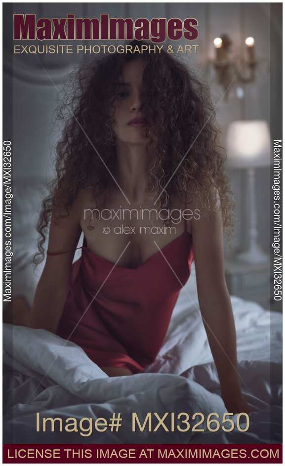 Sensual expressive portrait of a sexy woman with long curly hair in bed in dark bedroom