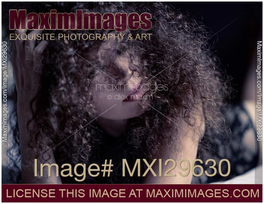 Sensual expressive portrait of a woman lying on a bed her face covered with long curly hair