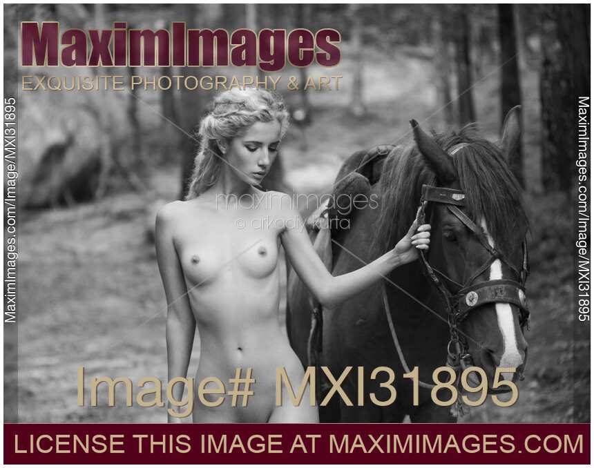 Sensual fine art black and white nude photograph of a young woman walking with a horse in the forest