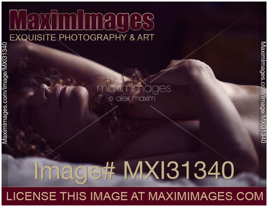 Sensual nude portrait of a woman lying naked in bed with her hand on her breasts