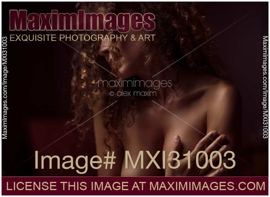 Sensual nude romantic portrait of a beautiful woman with long curly hair covering breasts in soft dim light