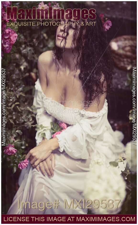 Sensual portrait of a beautiful woman in wet clothes sitting in rose garden in the rain