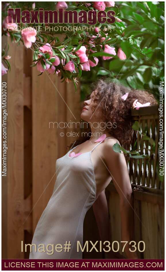 Sensual portrait of a beautiful woman leaning against a garden fence under a blooming camellia pink flowers
