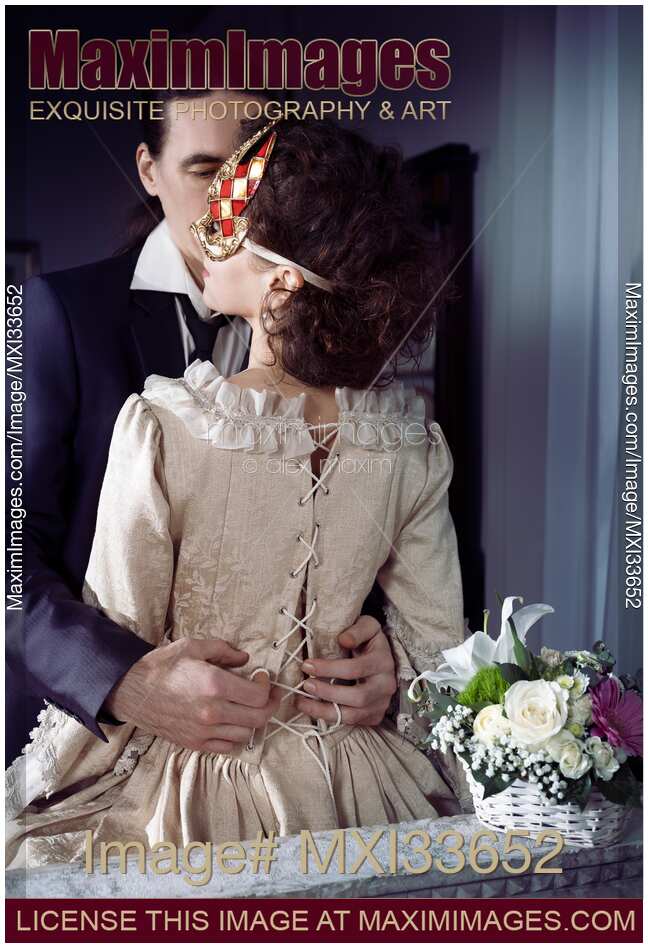 Sensual portrait of a couple, man unlacing corset dress back of a woman in Venetian carnival mask. Casanova romantic seduction concept.