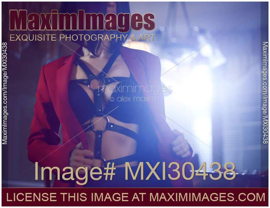 Sensual portrait of a sexy young woman taking off her suit jacket revealing black bondage leather harness over underwear in night