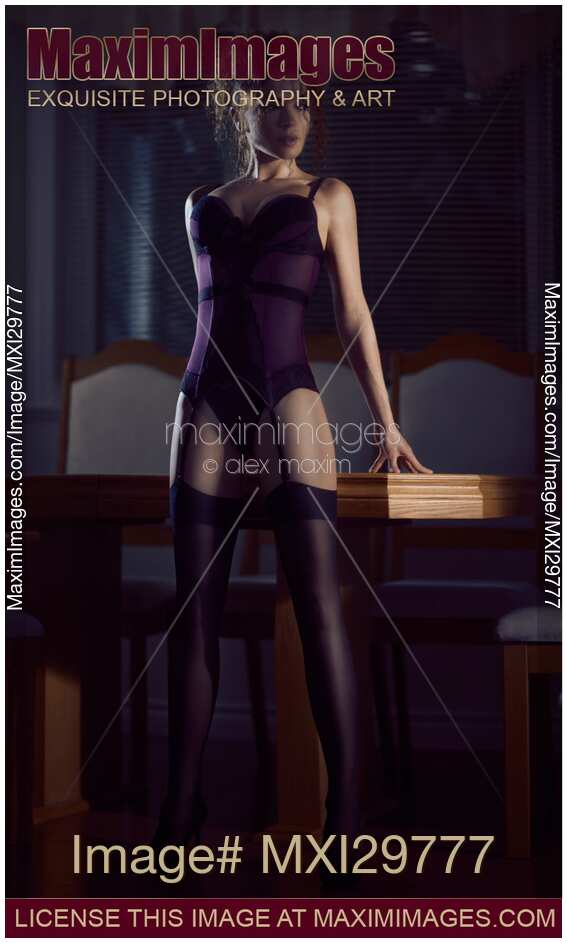 Sensual portrait of a woman in a corset and stockings leaning against a table in a bold pose
