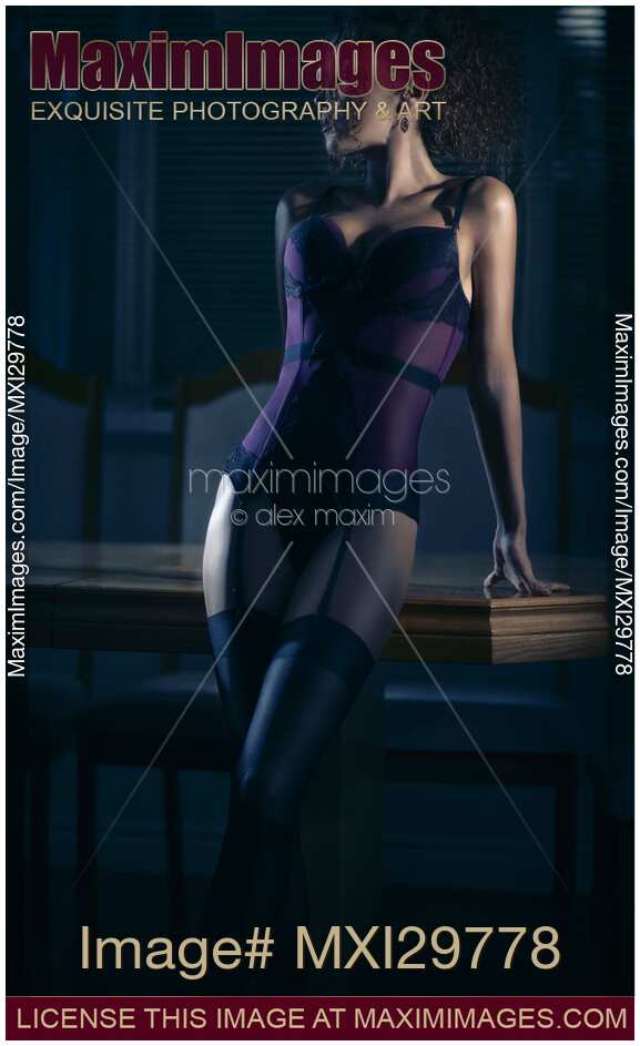 Sensual portrait of a woman in a corset and stockings leaning against a table