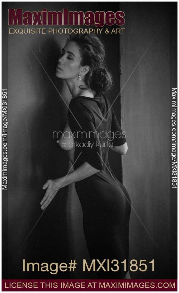 Sensual portrait of a woman in black dress revealing her bare breast leaning against a wall