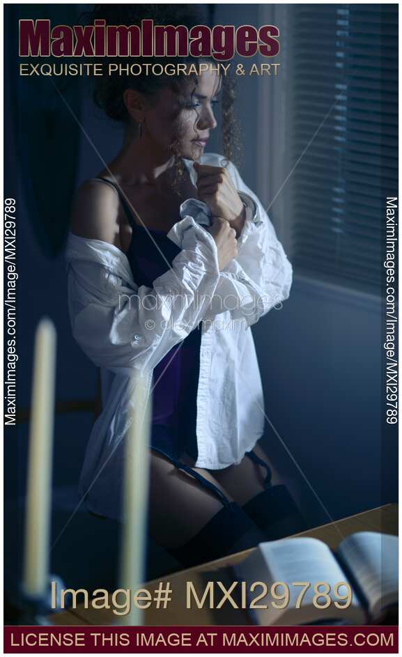 Sensual portrait of a woman in mens shirt and sexy corset sitting by the window with thoughtful expression